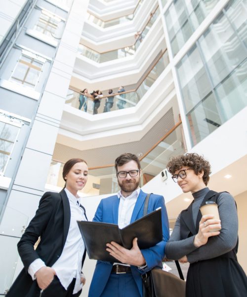 Below view of content young business team standing in office center and discussing data while analyzing papers